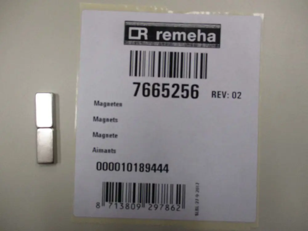 Magneten von Remeha auf einer Etikette, die die Artikelnummer 7665256 zeigt. Neben dem Etikett liegt ein magnetischer Bauteil in einer einfachen Form.